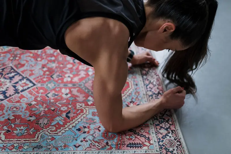 Woman performing a plank exercise on a patterned rug, showcasing muscular strength and focus