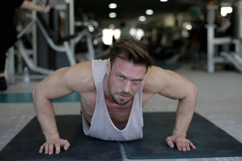 Determined adult muscular male athlete wearing sportswear performing handstand push up exercise during fitness workout on floor of modern spacious sport club an