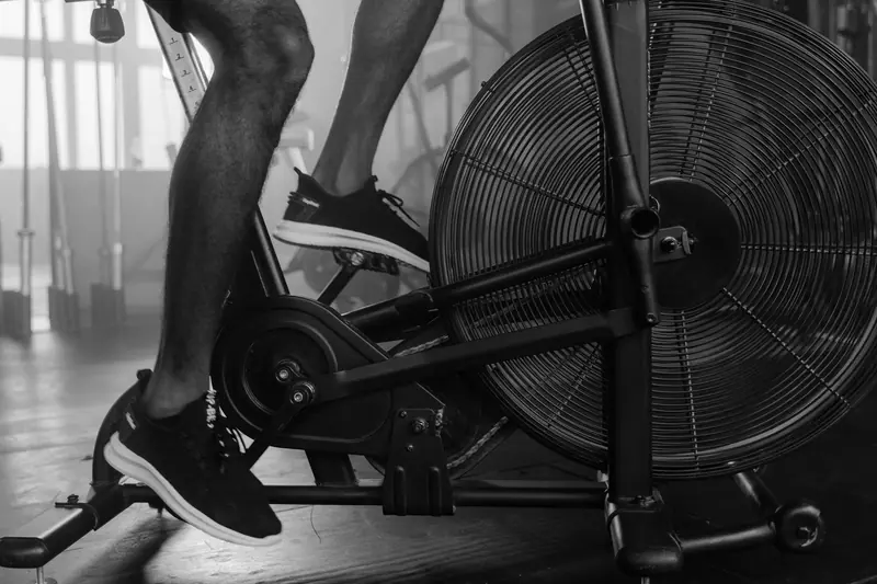 Black and white image of person using exercise bike in a gym setting
