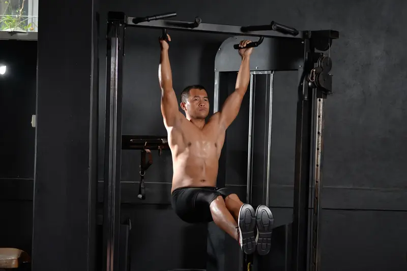 A shirtless man doing a workout with pull-up bar indoors at a gym, showcasing fitness and strength