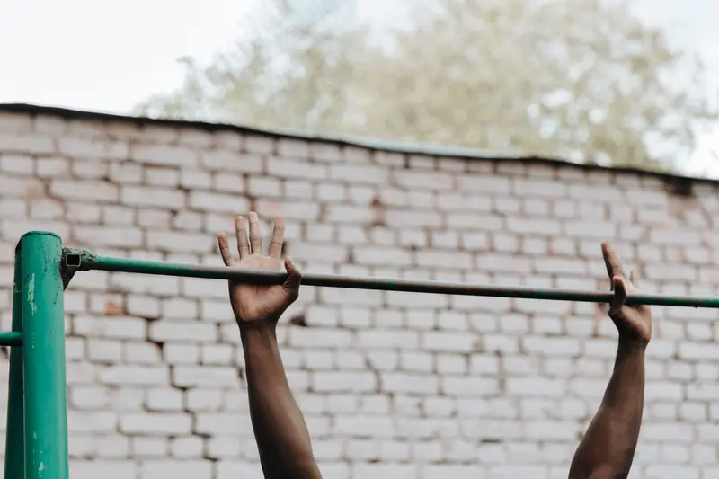 Hands of a person doing a pull-up on a metal bar against a brick wall