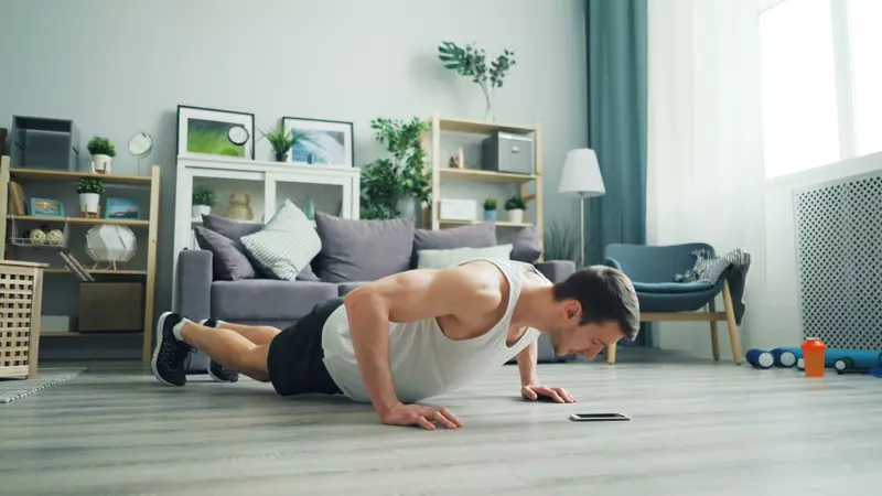 A muscular man performing push-ups in a modern living room, showcasing home fitness
