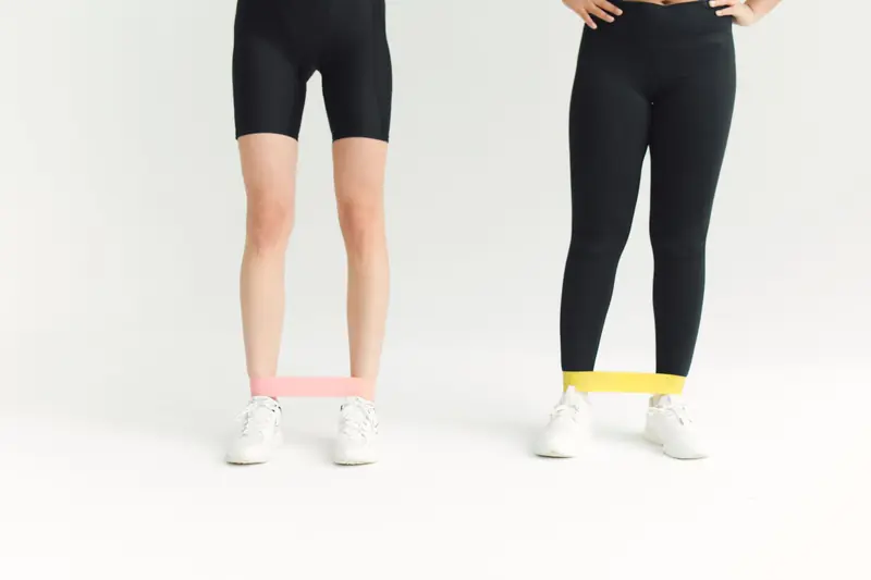 Two women in activewear using resistance bands during an indoor workout session