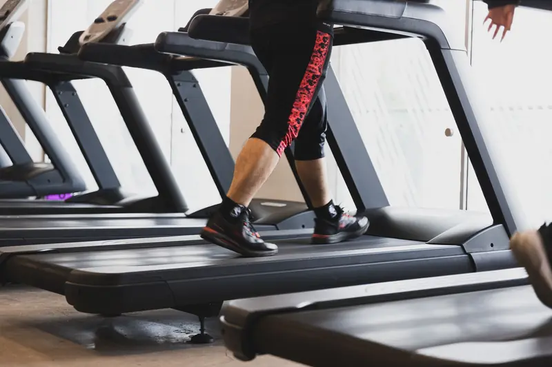 A person walking on a treadmill in a modern gym setting, focusing on fitness