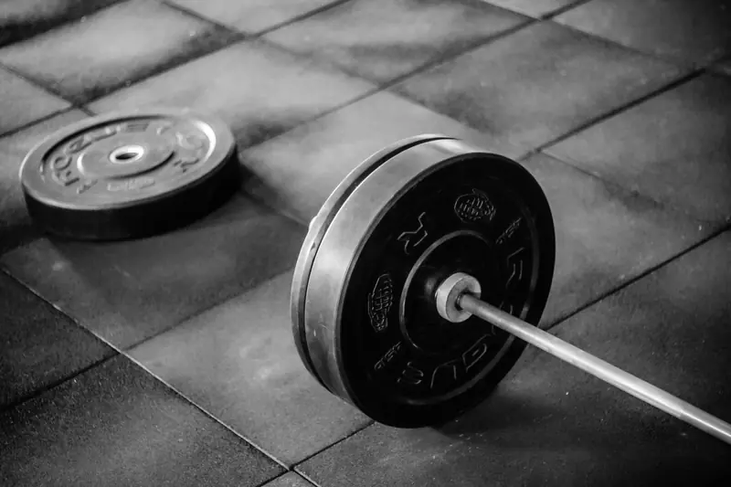 Grayscale image of heavy gym barbell and weights on rubber mat flooring