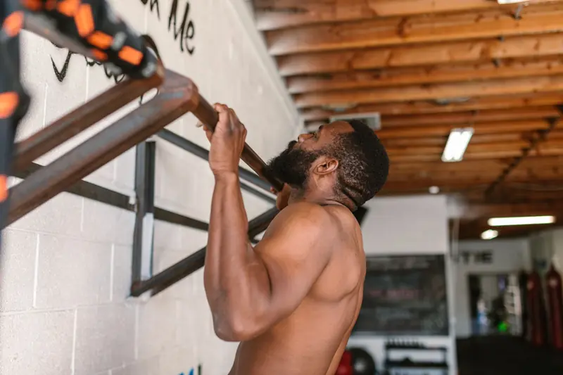 A shirtless man doing a pull-up exercise on a pull-up bar