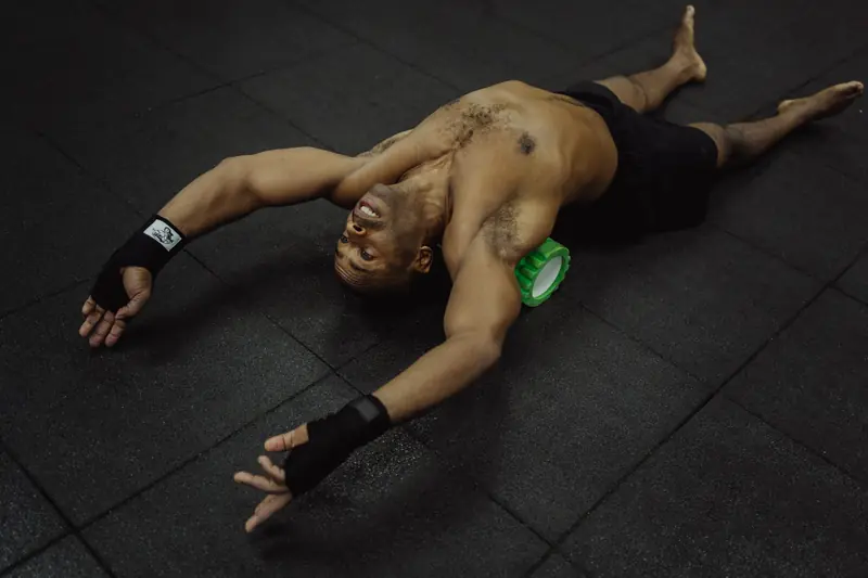 Topless man using foam roller for muscle recovery in gym setting